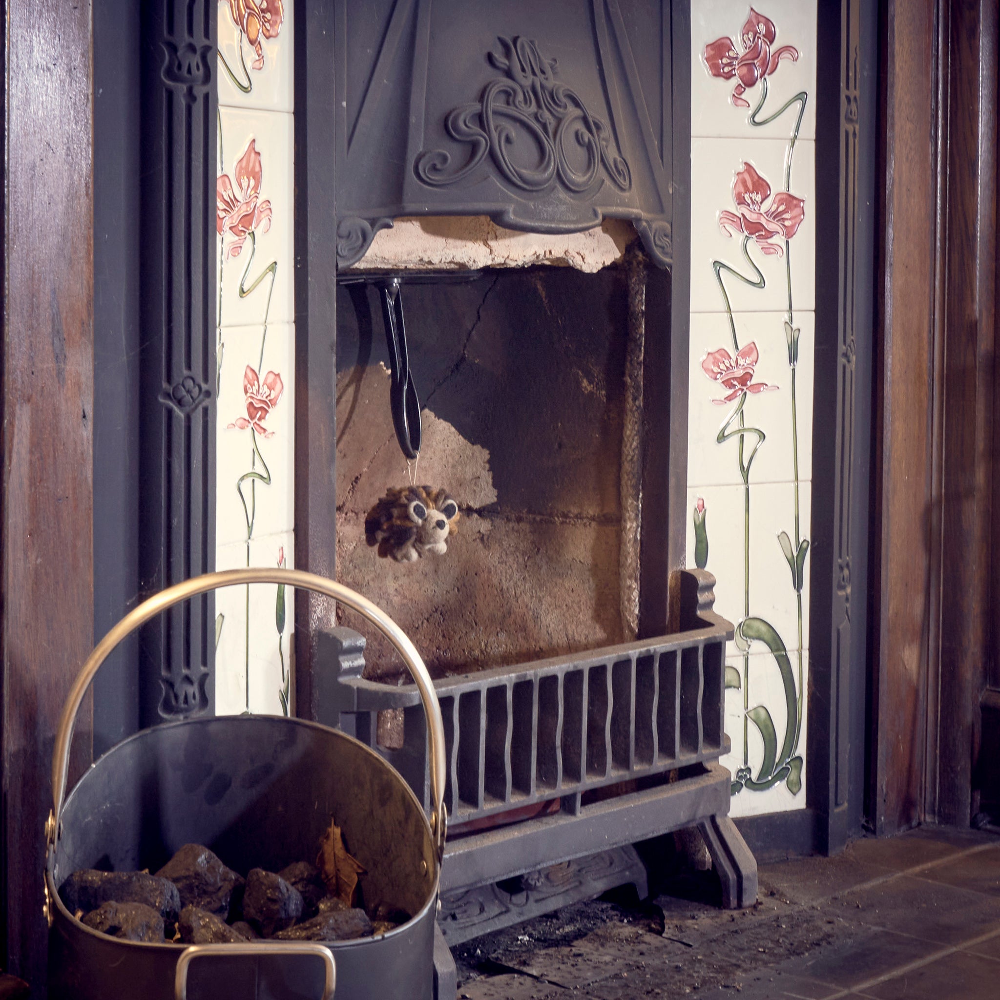 Fair trade woolly felted hedgehog hanging in Victorian tiled fireplace.