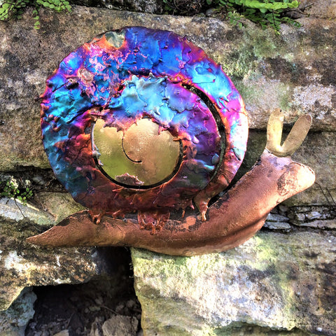 iridescent copper snail hanging on a garden wall