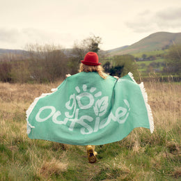 girl running through field with big towel made of recycled fibres and the logo Go Outside 