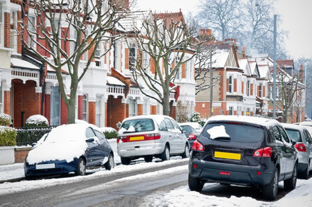 Snow fall on a typical british street showing houses and cars covered in snow.