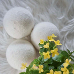 Wool dryer balls on a fluffy white background with natural flowers in front  thumbnail
