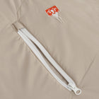 Close-up of a beige sleeping bag featuring a diagonal zippered pocket and a small red embroidered logo patch.