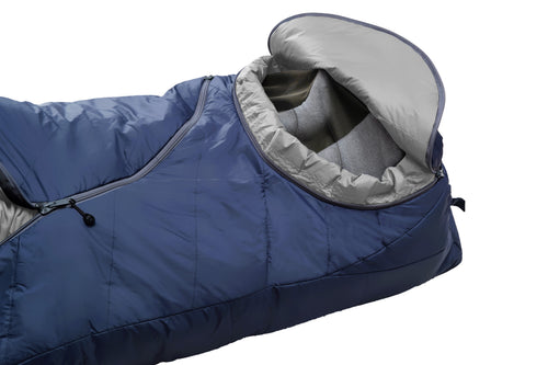 A dark navy blue sleeping bag with a gray interior lining, shown vertically against a plain white background. The sleeping bag features a zippered pocket on the upper side and a small red and white logo near the bottom.