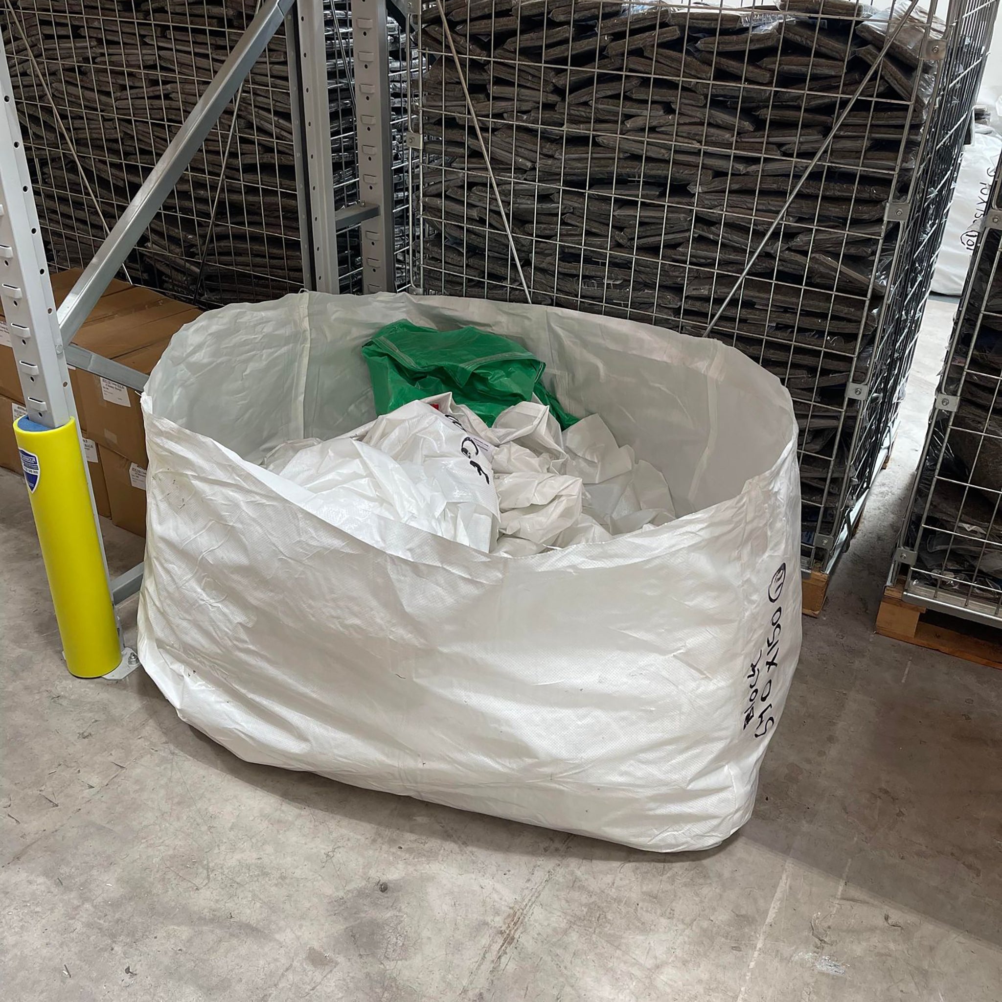 Big tarpaulin white bag being reused to store more bags on warehouse floor. 