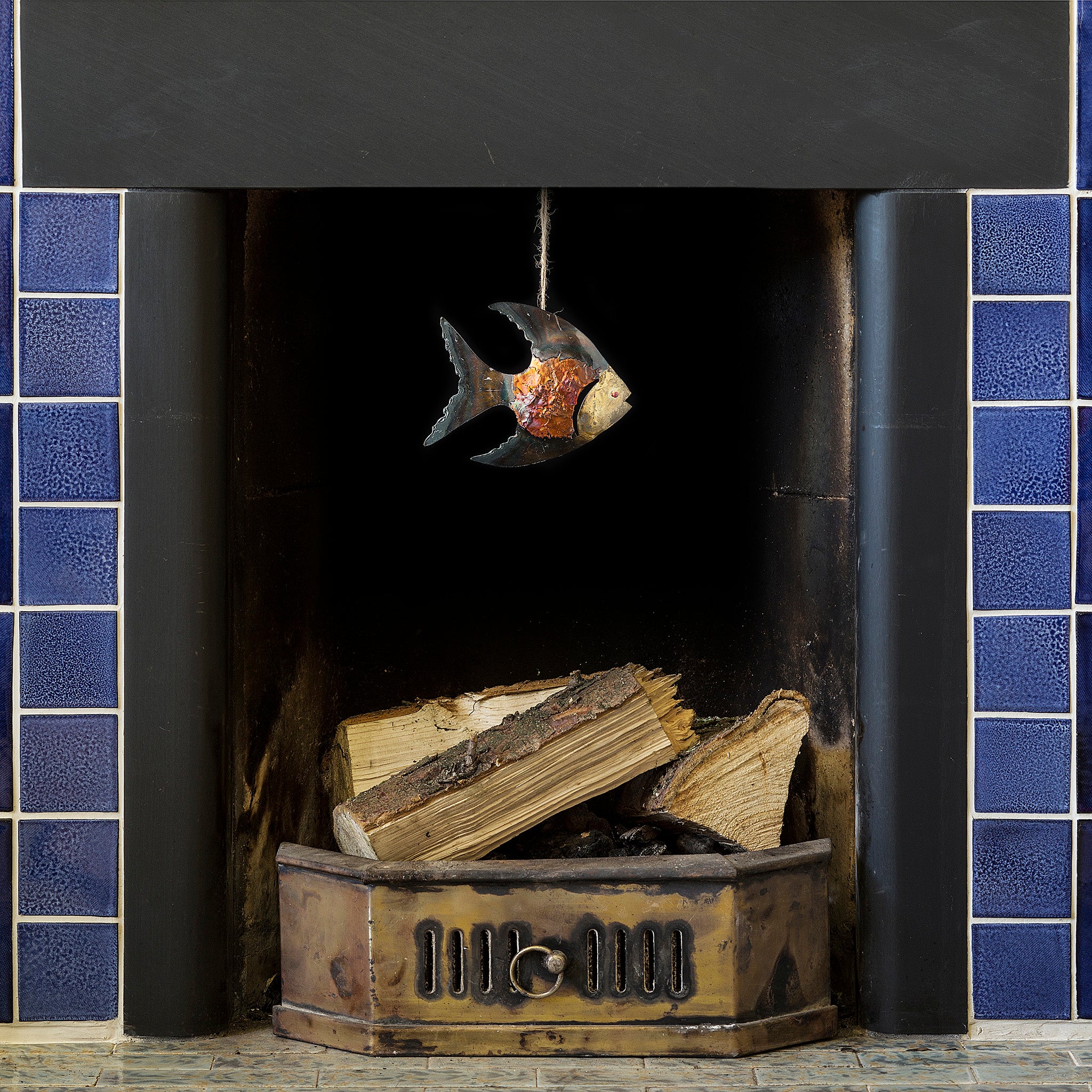 Iridescent copper and tin fish dangling from a blue tiled fireplace featuring vivid colours of copper and gold