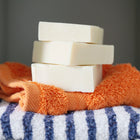 Stack of three Olive Oil Castile soaps stacked on an orange flannel on top of a navy blue and white striped towel