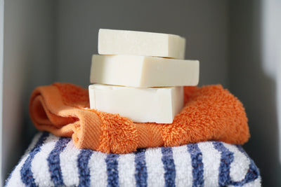 Stack of three Olive Oil Castile soaps stacked on an orange flannel on top of a navy blue and white striped towel