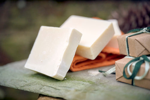 Stack of three Olive Oil Castile soaps stacked on an orange flannel on top of a navy blue and white striped towel