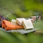 Three bars of white olive oil Castile soap, and three bars of castile soap gift-wrapped in natural outdoors surrounding