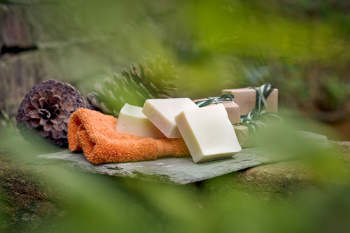 Stack of three Olive Oil Castile soaps stacked on an orange flannel on top of a navy blue and white striped towel