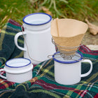 Portable wire coffee dripper with enamel mug and billycan on tartan picnic rug and autumn leaves