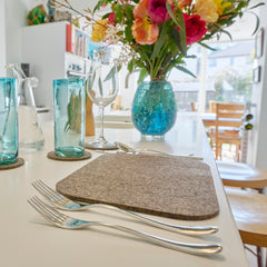 Chimney Sheep Lakeland collection grey wool felted tablemat and coasters on white countertop. Zoomed in on tablemats and blue glasses thumbnail