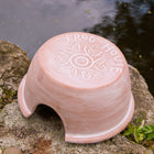 Ceramic frog house with 'Frog House' engraving on a stone surface near water.