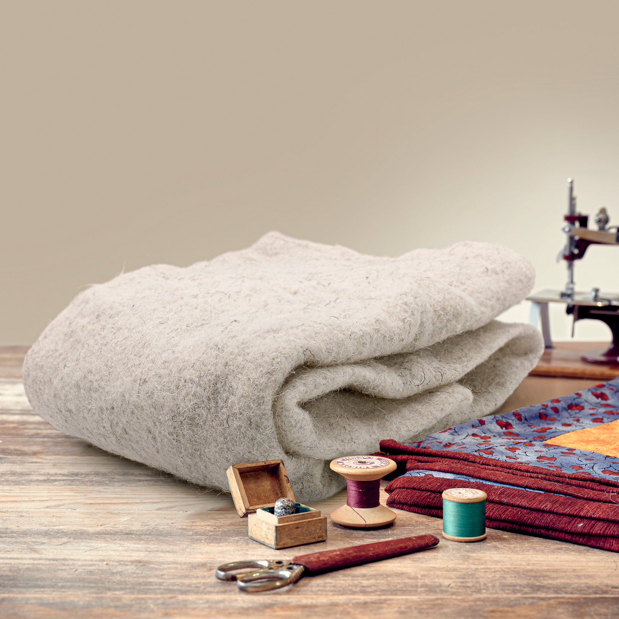 Wadding on a wood desk with cotton spools thimble and scissors with a sewing machine in background
