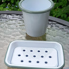 White enamel soap dish and mug with sage green rim on glass table
