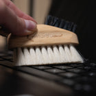 Hand holding a wooden brush with natural fibers over a keyboard