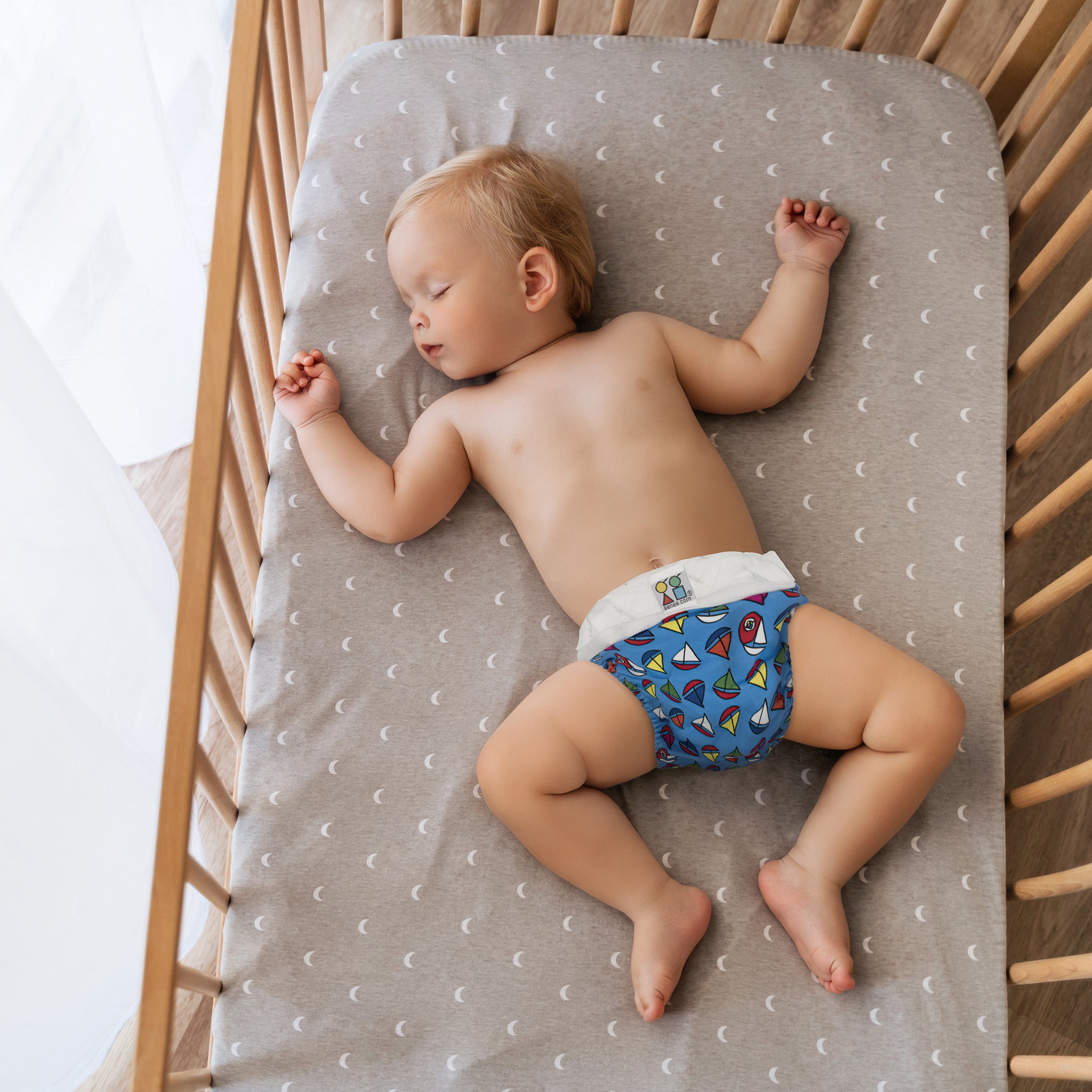 Baby asleep wearing blue hybrid nappy pants with sailboat design