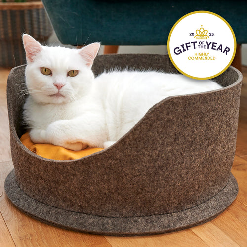 White cat lying in a grey felt pet bed with a 'Gift of the Year Highly Commended' badge.