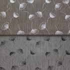 A close-up of a gray patterned fabric with a fine herringbone texture, featuring a white and black flower pattern.