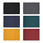 A variety of Chimney Sheep woollen rollup travel dog beds sit upon a white background. There are six woollen flat dog beds in the image. The rectangular wool dog beds are in a variety of colours. There are six colours: Black, grey, blue, green, yellow and red.