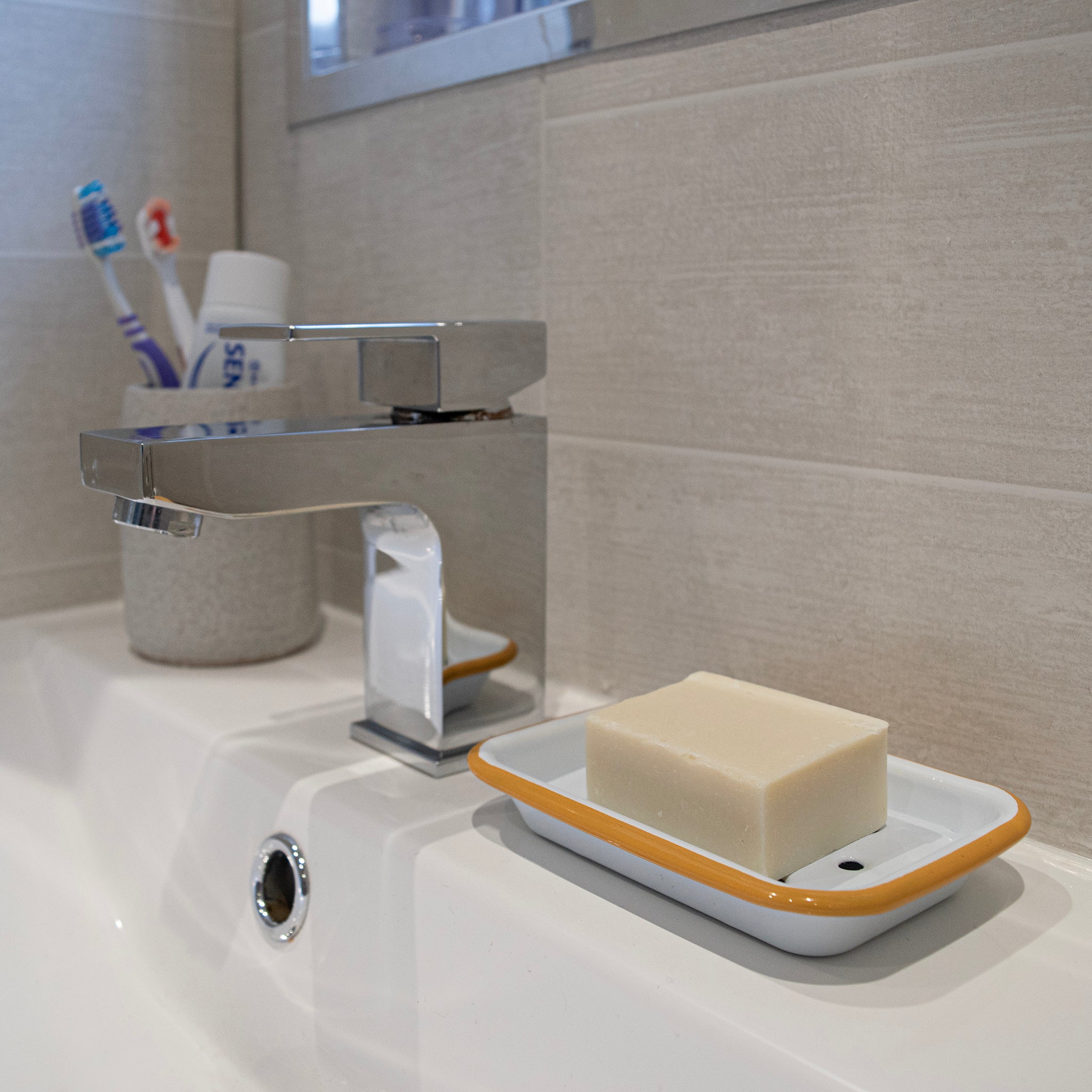 Bathroom sink with soap dish, bar of soap, and toothbrush holder.