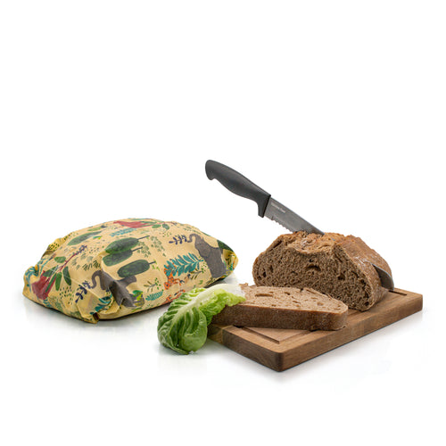 A pack of Beeswax Wraps from Chimney Sheep, showing the brown kraft paper packaging and a single reusable beeswax wrap with a colourful wildflower and animal pattern on a cream background.