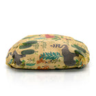 A loaf of bread wrapped in a beeswax wrap with a whimsical safari animal print on a warm yellow background, featuring green foliage, a grey elephant, and an orange tiger, photographed on a clean white background with a soft reflection.