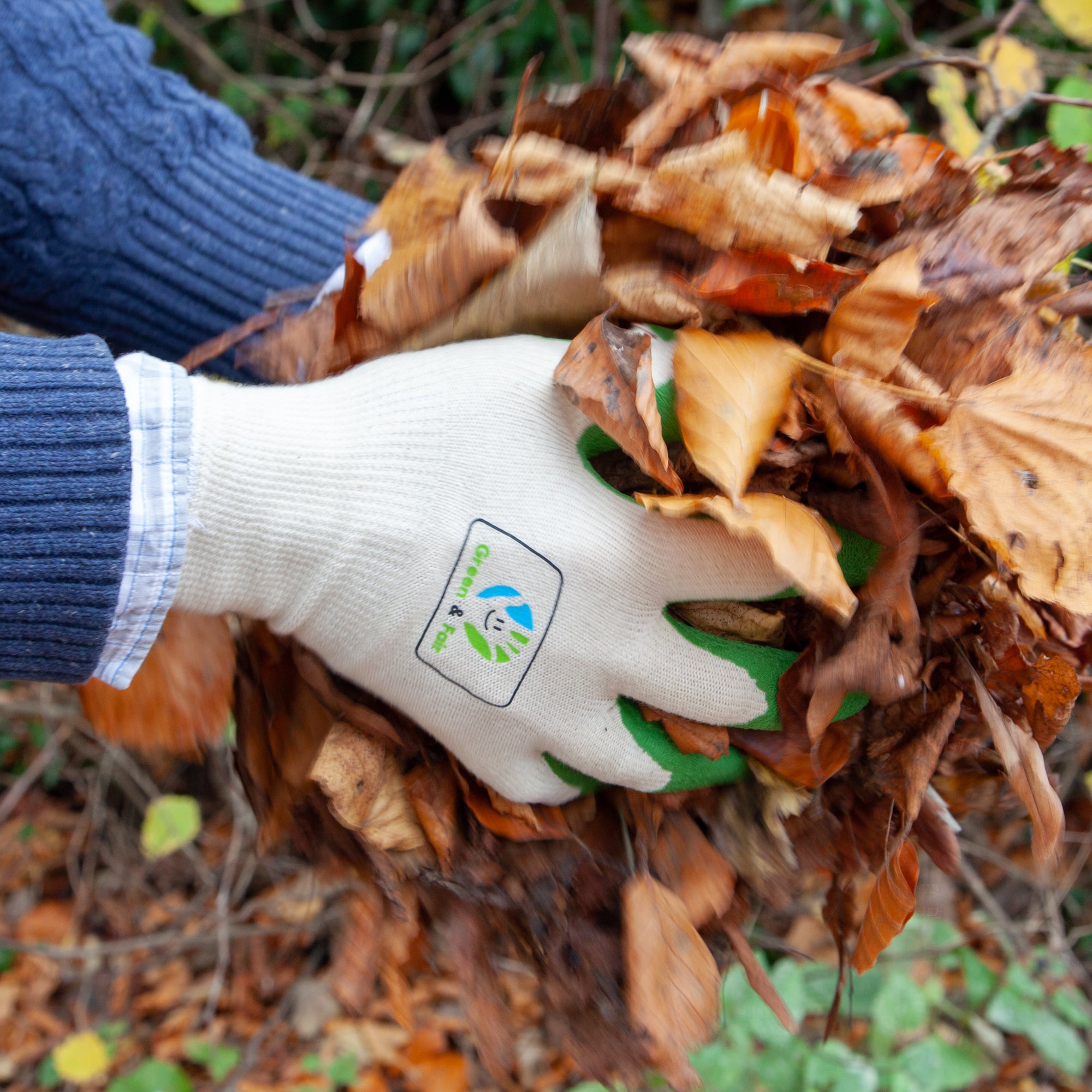Hand wearing a white gardening glove with a logo, holding a handful of autumn leaves.