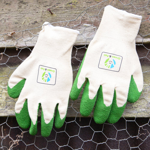 Gardening gloves with green fingertips on a wooden surface with gardening tools in the background.
