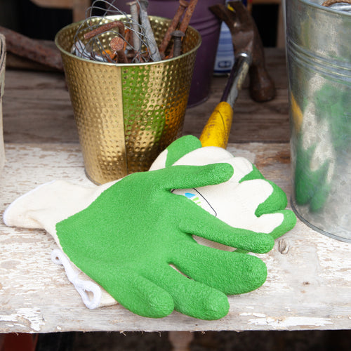Gardening gloves with green fingertips on a wooden surface with gardening tools in the background.